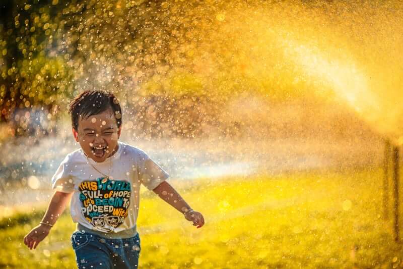 child running through sprinkler for benefits of water play in early childhood